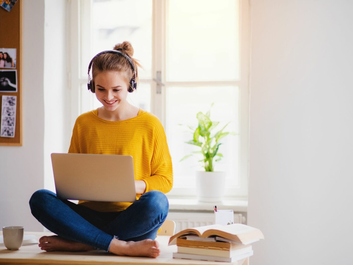 Hymyilevä nainen istumassa tietokone sylissään ja kuulokkeet korvissa.